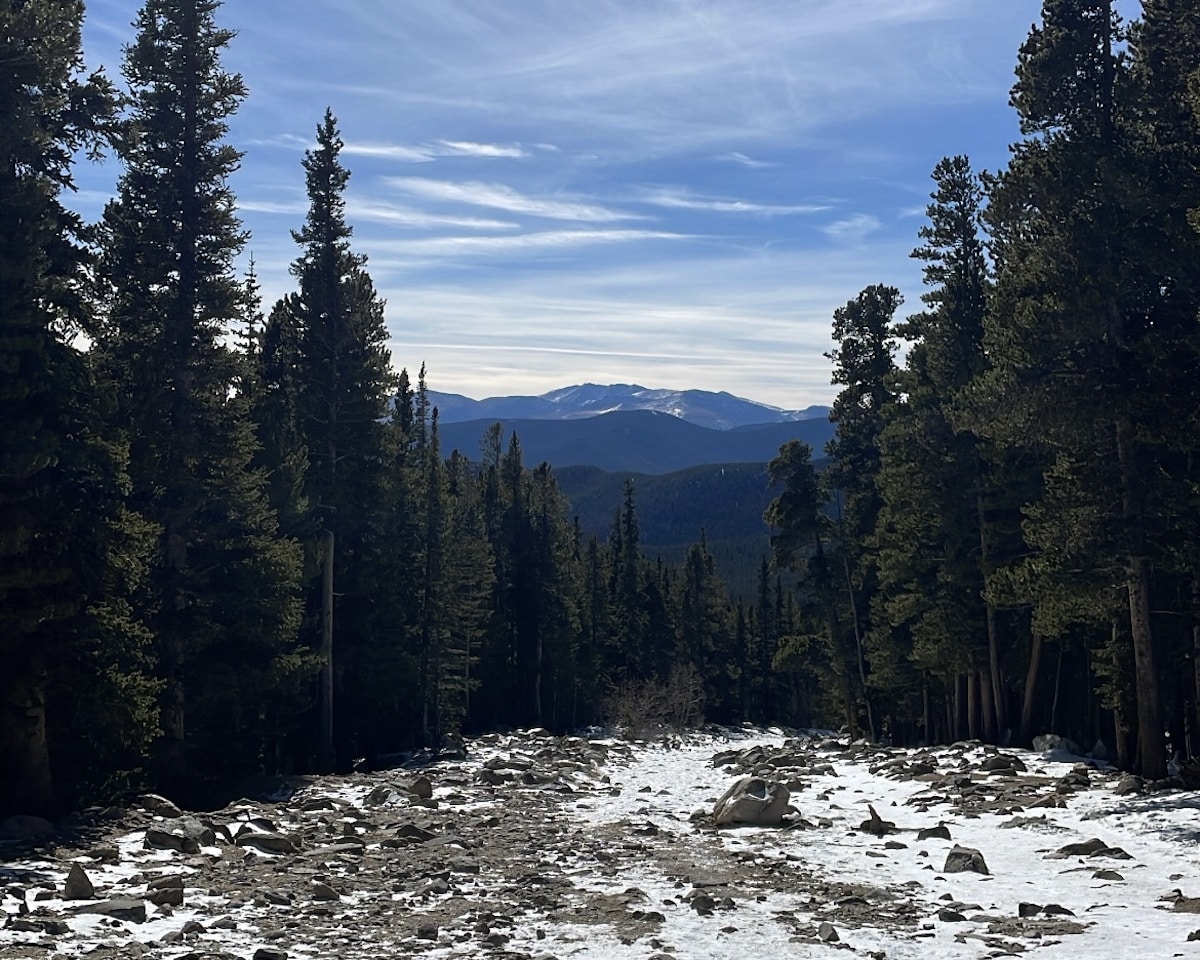 A Colorado trail with snow and mud. There are trees and a view of mountains.