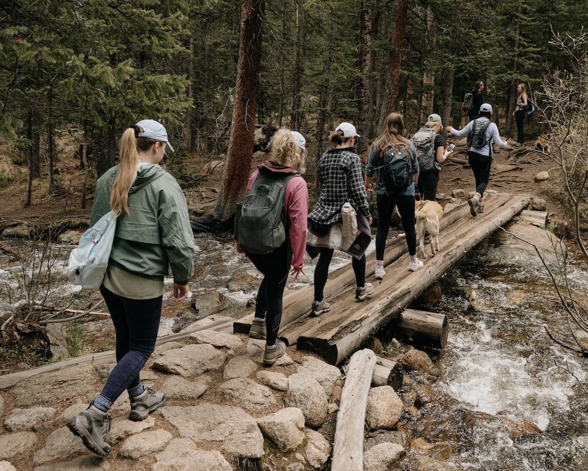 Group of female hikers crossing a bridge over water on a trail in Colorado