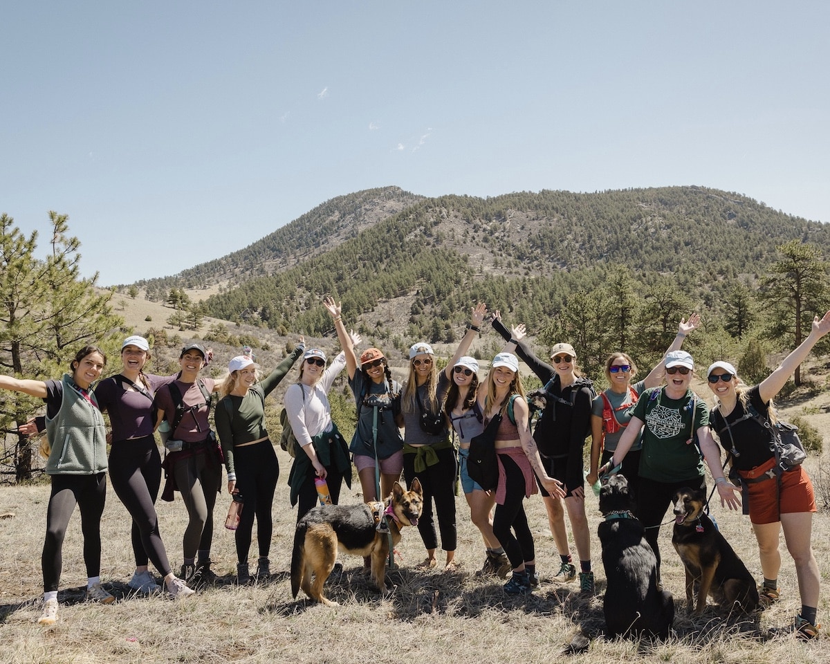 A group of women hiking and posing for a photo in a meadow with a mountain behind in Colorado