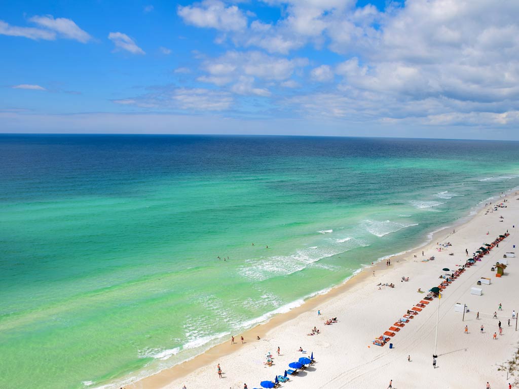 An aerial view of turquoise waters and a white sand beach dotted with beachgoers in Destin, Florida on a sunny day