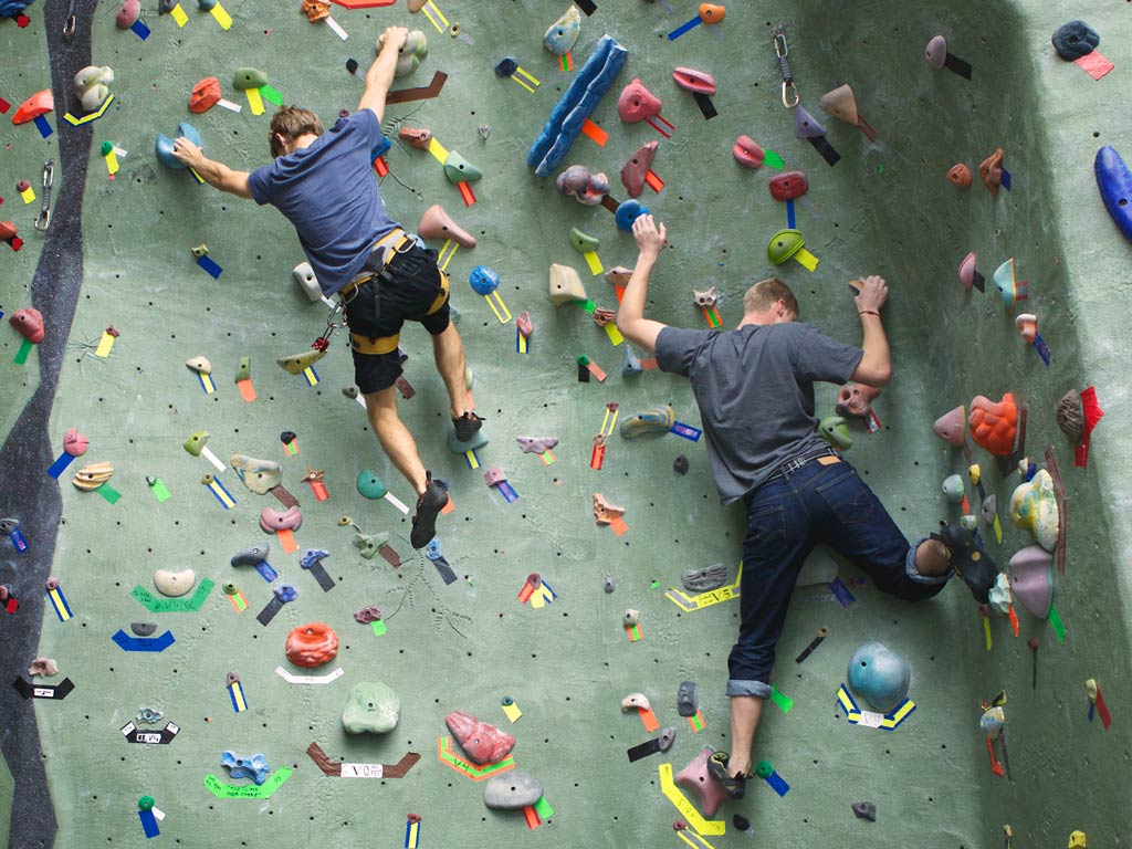 A photo featuring two rock climbers doing their best to overcome obstacles as they climb an indoor wall