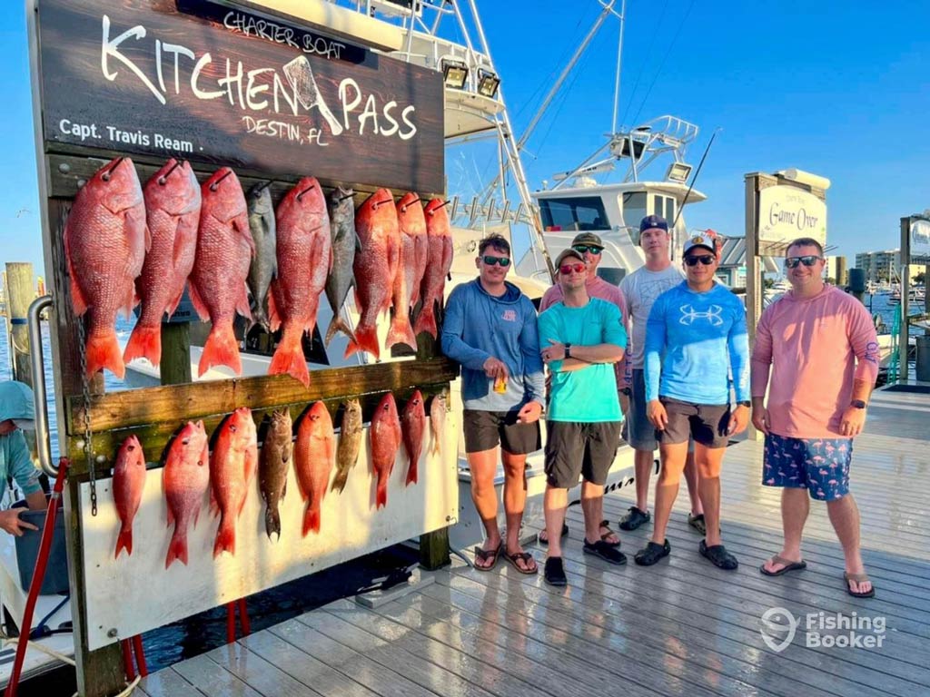 A photo featuring five anglers standing on a dock next to a fish rack full of Snapper after their fishing trip in Destin