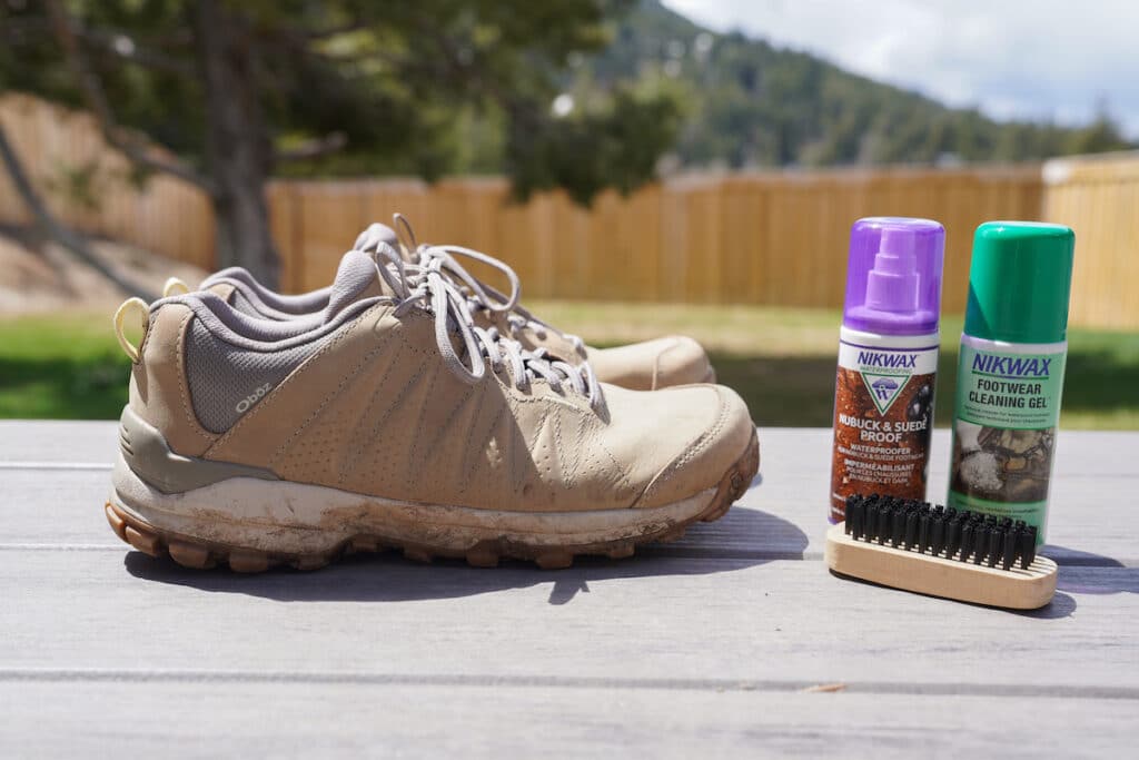 pair of dirty hiking boots on a deck. Nikwax footwear cleaning gel and waterproofing spray are next to the shoes