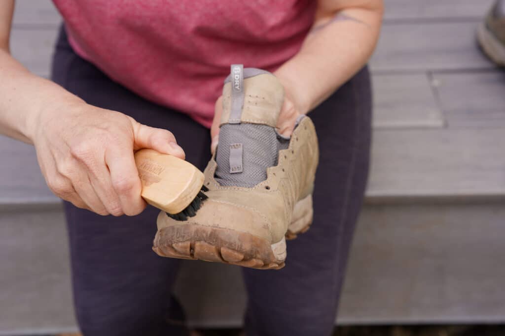 woman brushing dirt off hiking boots with a brush