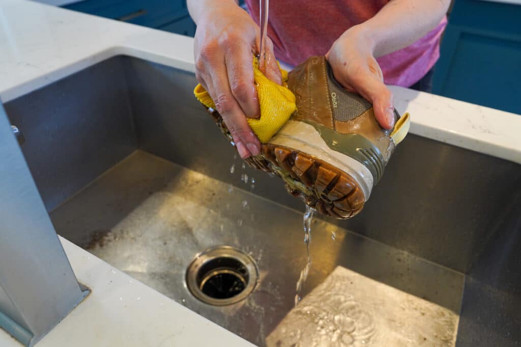 woman wiping down hiking boot with a microfiber cloth under kitchen faucet