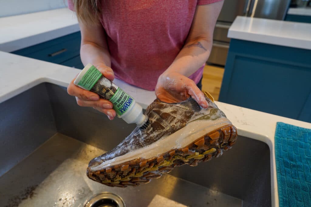woman cleaning hiking boots in kitchen sink with nikwax footwear cleaning gel