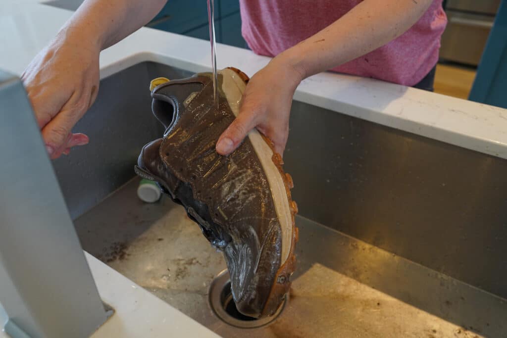 woman rinsing nikwax cleaning gel off hiking boot under kitchen faucet