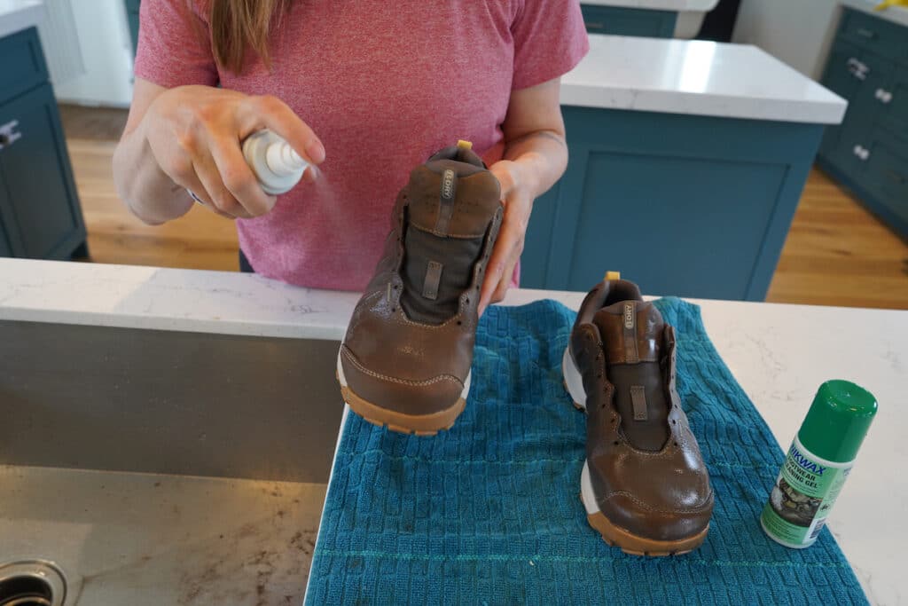woman spraying clean, wet hiking boots with Nikwax waterproofing spray