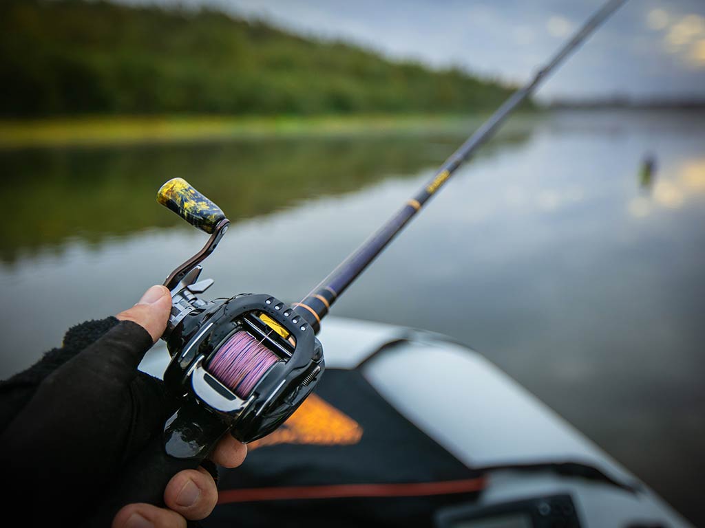 A closeup of the reel of a baitcasting fishing setup, with a thumb visible working the reel against a blurred background