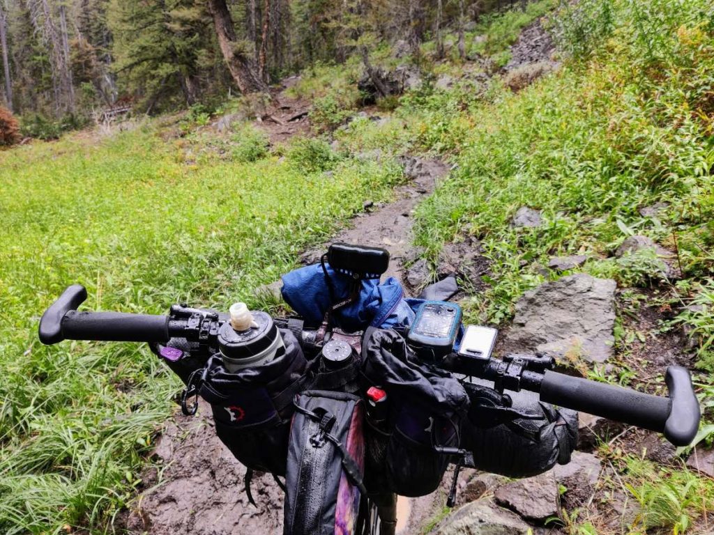 Looking over mountain bike handlebars to muddy trail