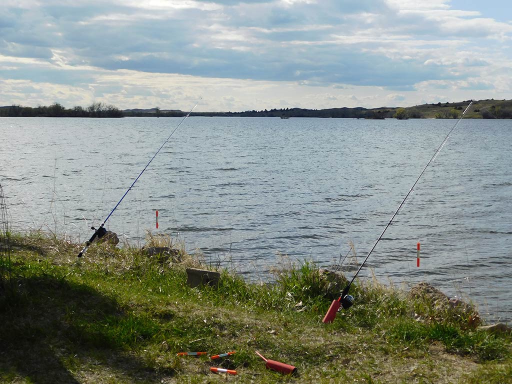 Two fishing rods set up from the shore of a wide lake in Nebraska at sunset on a cloudy day