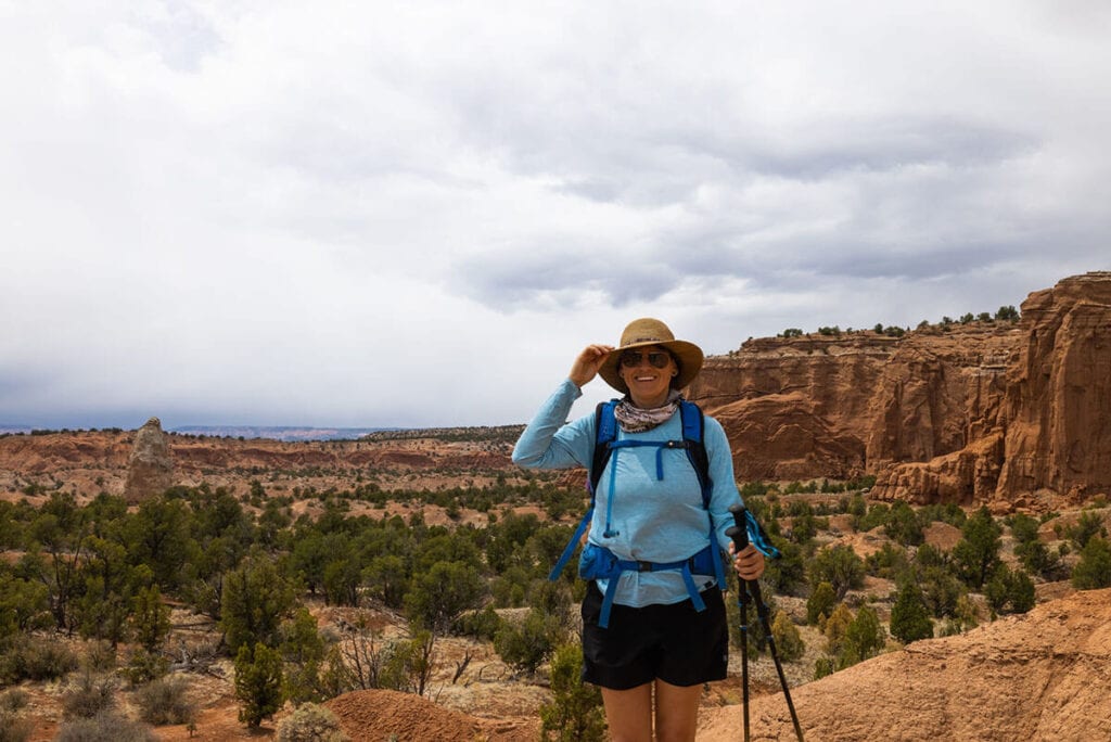 Kristen Bor dressed in hiking gear and holding trekking poles on trail in Kodachrome Basin in Utah with red rock landscape behind her