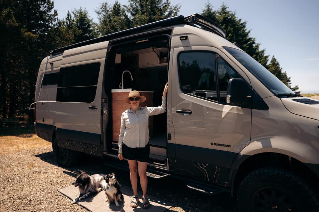 A woman stands outside of her Sprinter van with the side door open wearing Outdoor Research Astroman Long Sleeve Sun Shirt