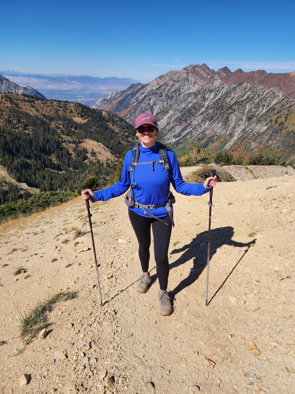 Kristen Bor hiking at the top of Snowbird Ski Area with mountains and Salt Lake Valley in the background. She is wearing the Outdoor Research Echo Hoody sun protection shirt