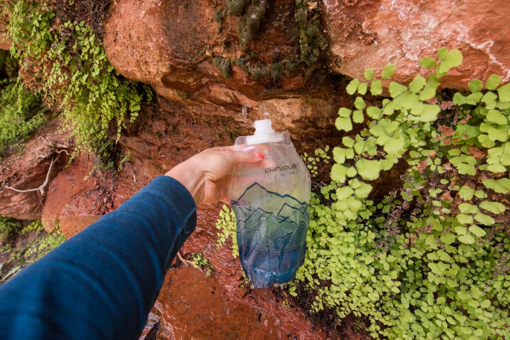 A hand holding up a water bottle under a natural desert spring