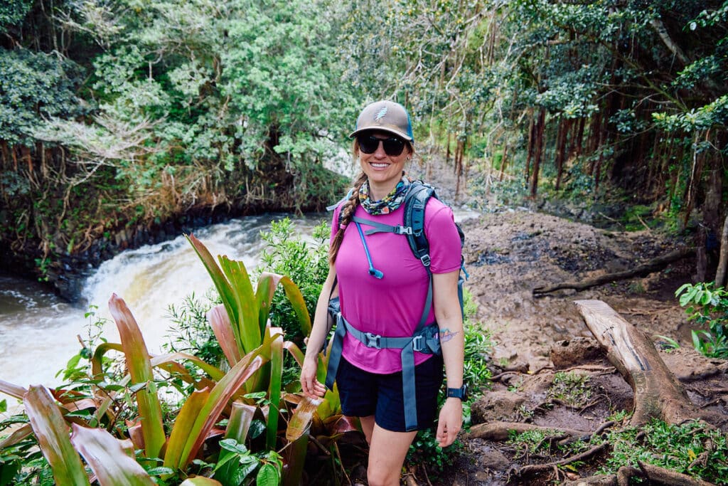A woman stands on the Twin Falls Trail hiking trail in Maui. She is wearing a pink lululemon shirt and black North Face Aphrodite Motion Shorts