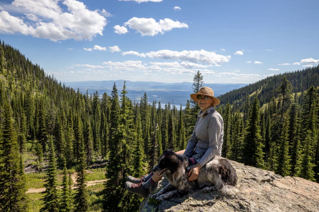 Kristen Bor sitting with her dog on a rock along a hiking trail with views of Whitefish Lake in Montana