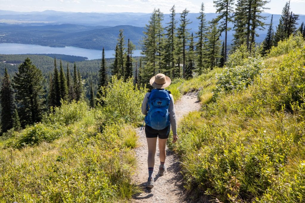 Woman hiking away from camera on trail looking out over a lake and mountains
