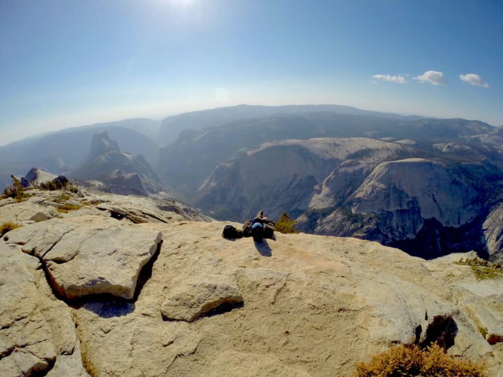 Man laying down on rocks at the top of Clouds Rest looking down on Yosemite national Park