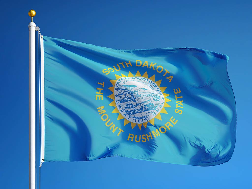 The flag of South Dakota flying from a flagpole against a background of a clear blue sky