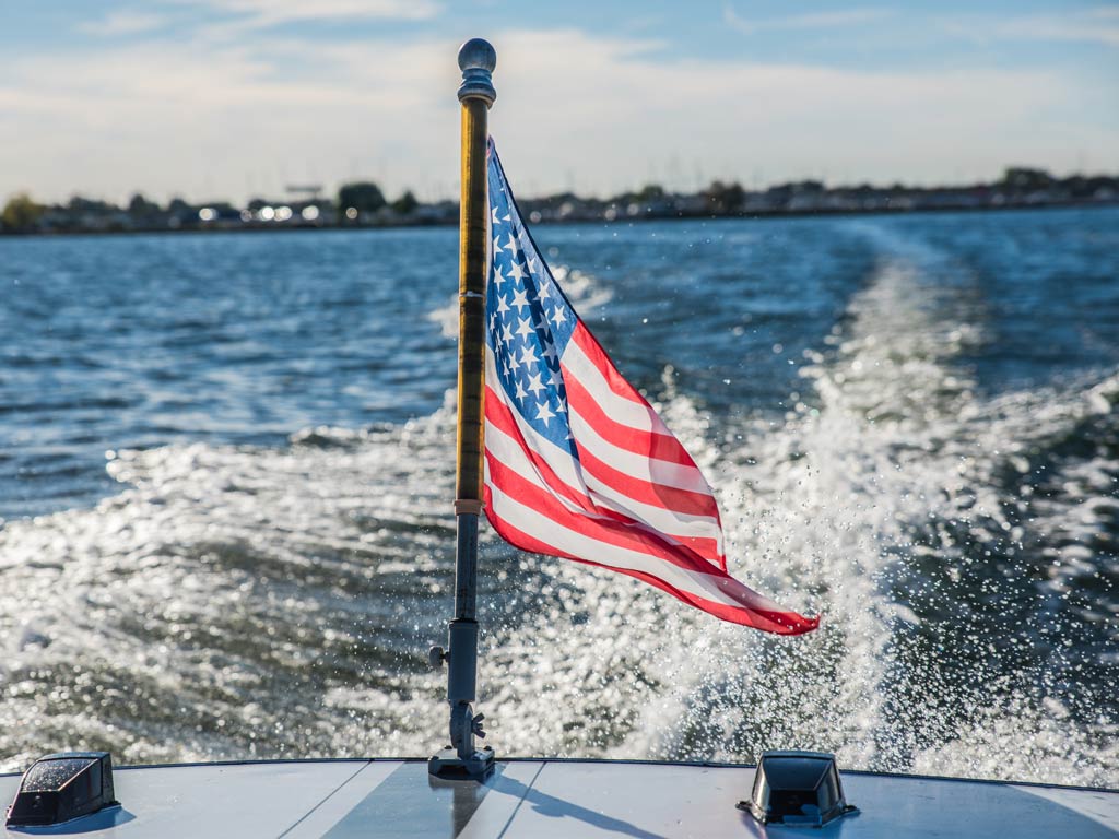 A photo featuring a wind-borne American flag on a charter while the boat is moving away from the shore on a Memorial Day fishing trip