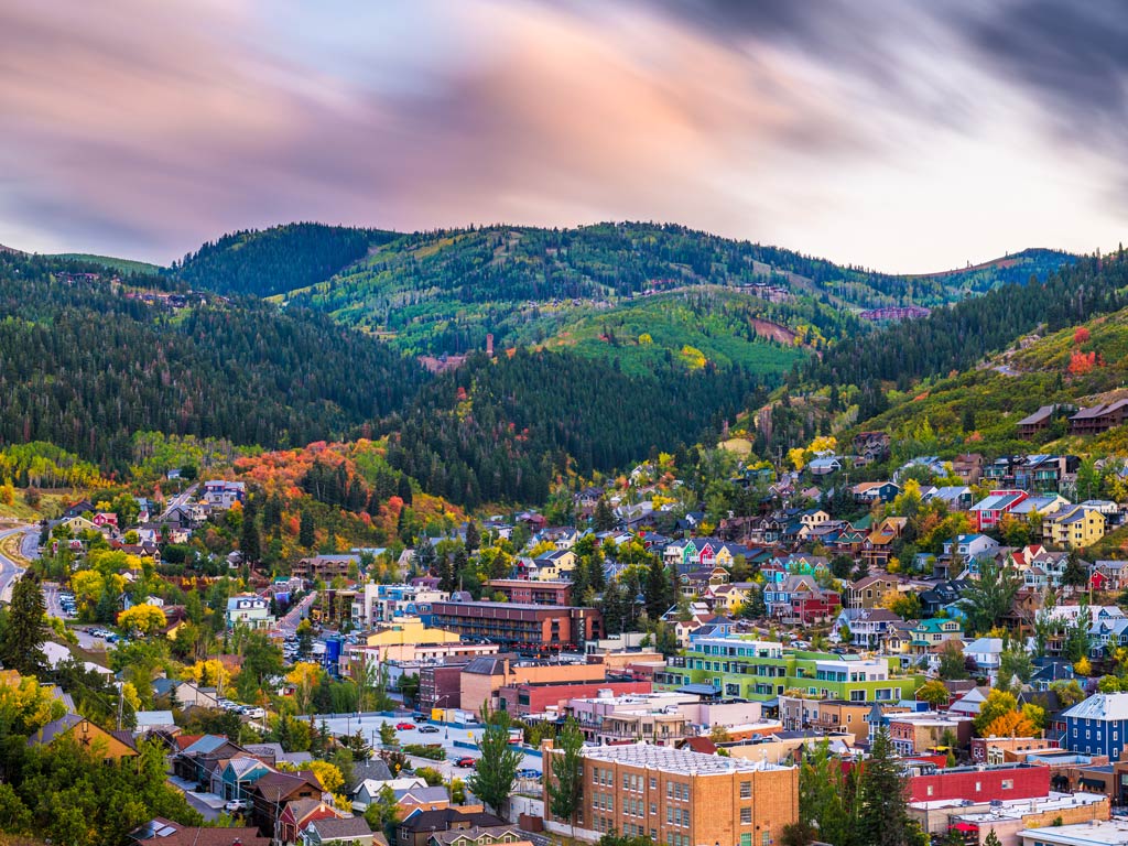A photo featuring scenic city of Park City dotted with colorful buildings and houses surrounded by mountains  at dusk