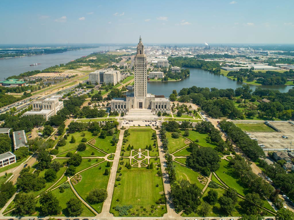 An aerial view of the Louisiana State Capitol surrounded by greenery and fishable blue waters of Baton Rouge on a bright spring day
