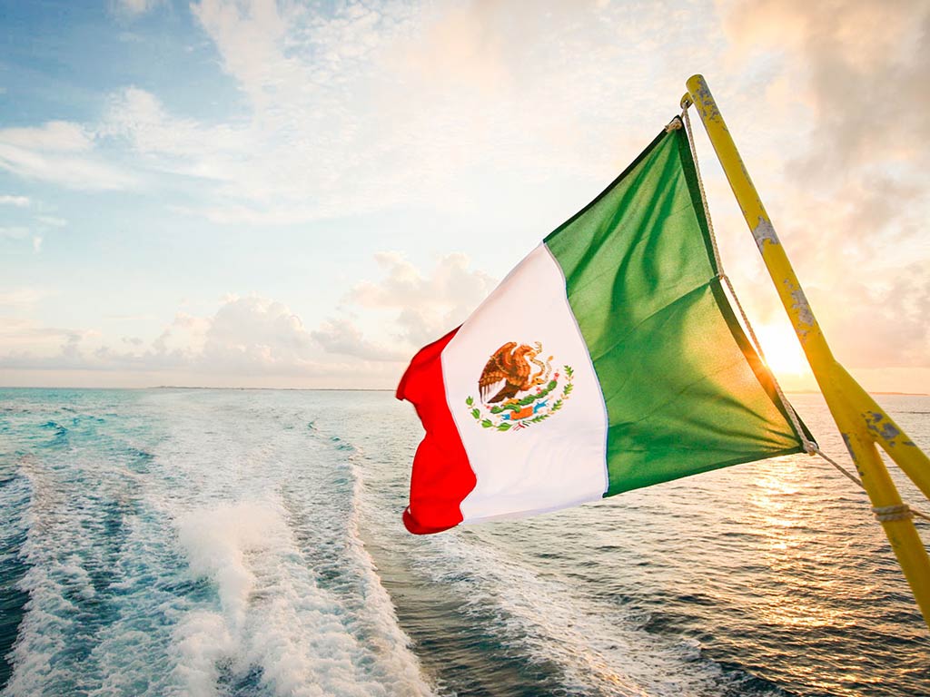 A Mexican flag flutters in the wind on the back of a boat heading out to the deep offshore waters