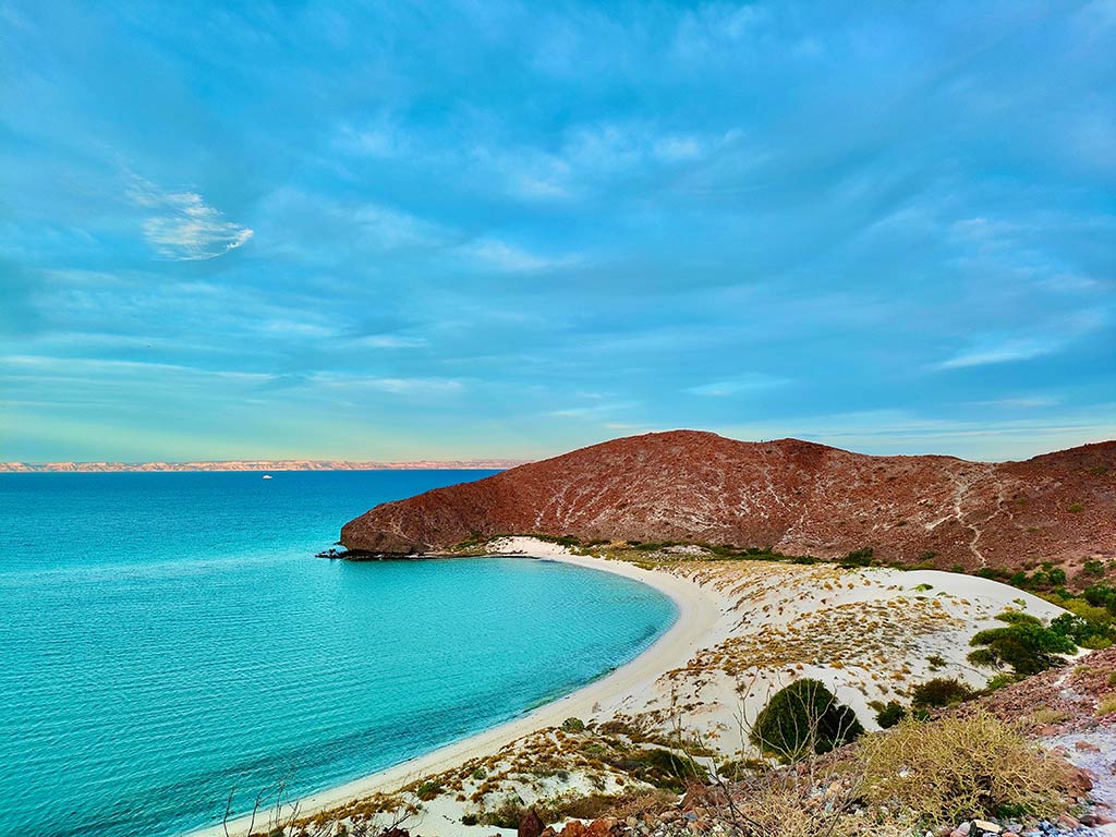 A view from a hill towards a deserted Balandra Beach in La Paz, Mexico with clear skies at the end of the day and crystal clear waters visible on the left of the image