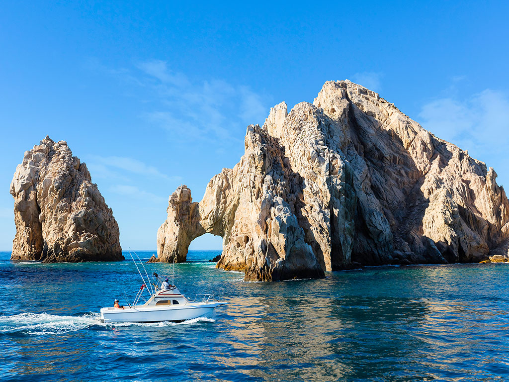 A fishing boat sails past the famous arch in Cabo San Lucas on a sunny day