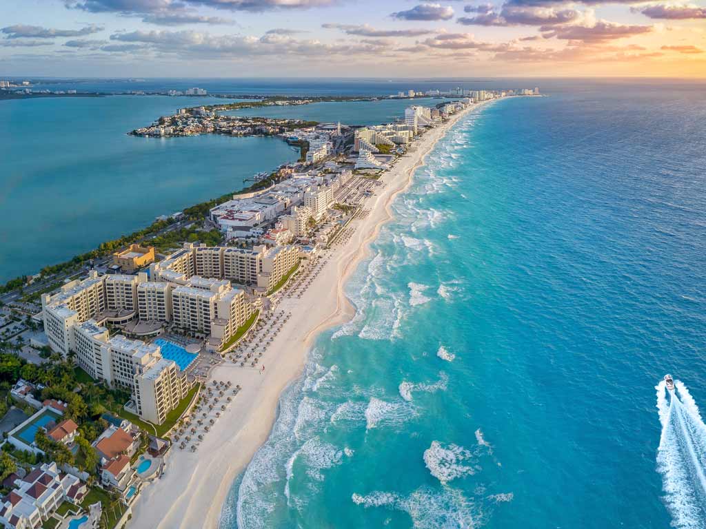 A scenic aerial shot of the coast of Cancún at sunset, with waves crashing against the city's sand beaches.