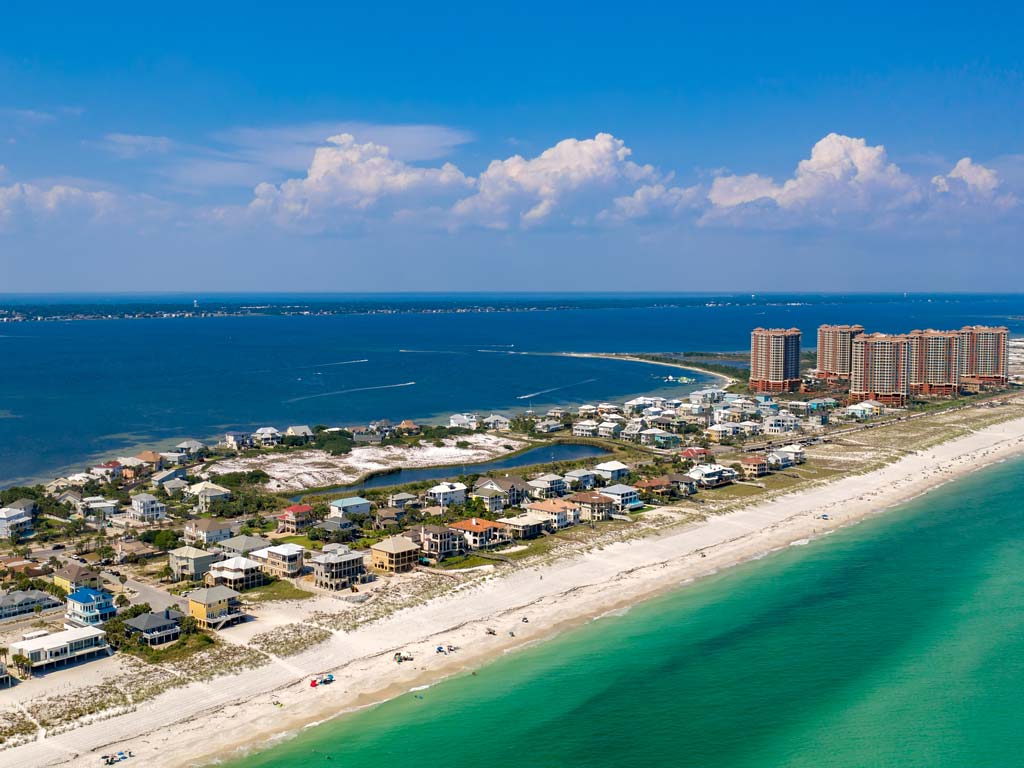 An aerial shot of Pensacola Beach near the city of Pensacola, which is one of the best Red Snapper fishing spots in the Gulf, with emerald green waters in the foreground while the darker waters of the bay are visible in the background.