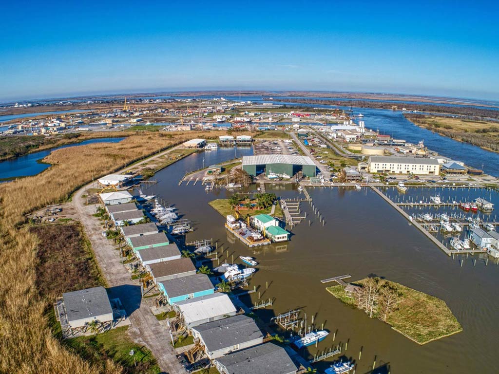 An aerial view of Venice, Louisiana, with various houses, warehouses, and marina docks dotted with charter fishing boats visible.