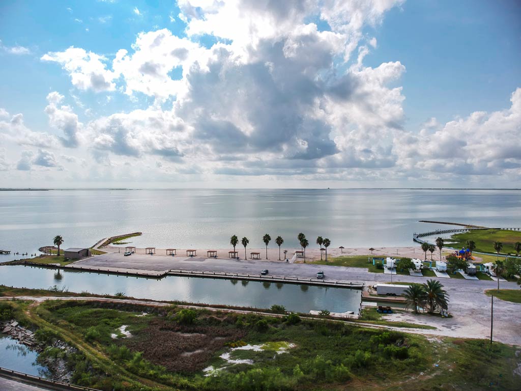 An aerial view of the bay in Port Lavaca, Texas, with calm waters stretching towards the horizon and cumulus clouds in the skies.