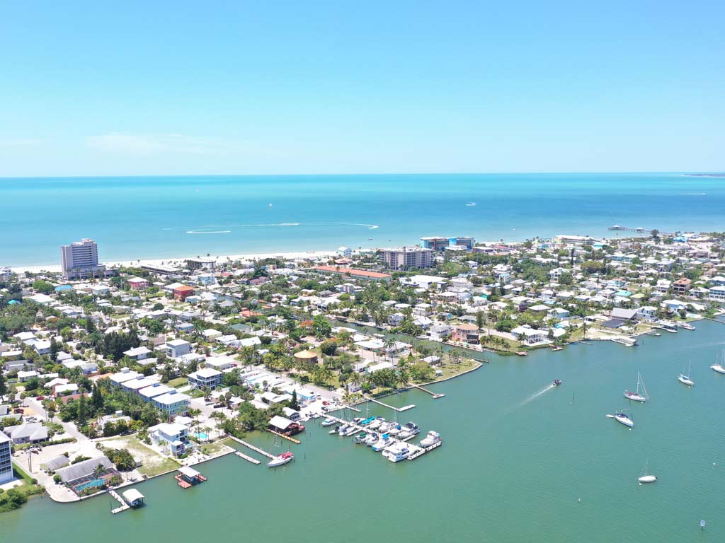 An aerial photo of Fort Myers Beach, one of the best Red Snapper fishing spots, on a clear, sunny day, with light blue bay waters visible in the foreground, with the Gulf of Mexico stretching in the background.