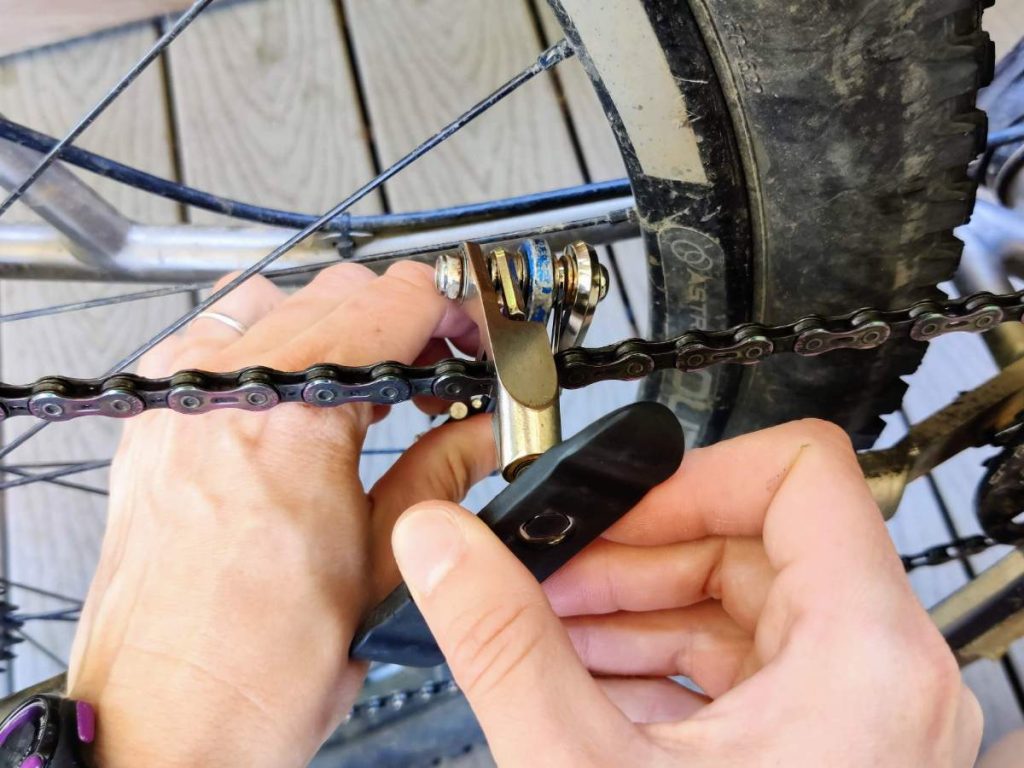 Close up of hands about to split bicycle chain using multitool chain breaker