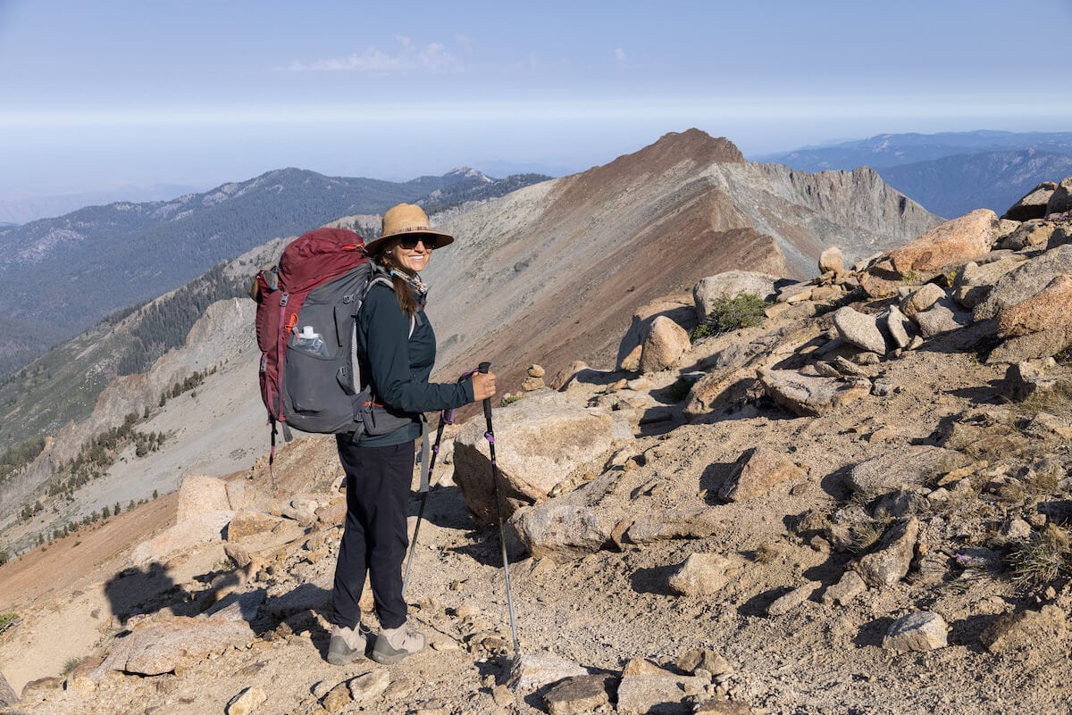 Kristen Bor smiles wearing a red backpacking pack on top of a rocky ridge wearing Mountain Hardwear Dynama Ankle Pants in Sequoia National Park