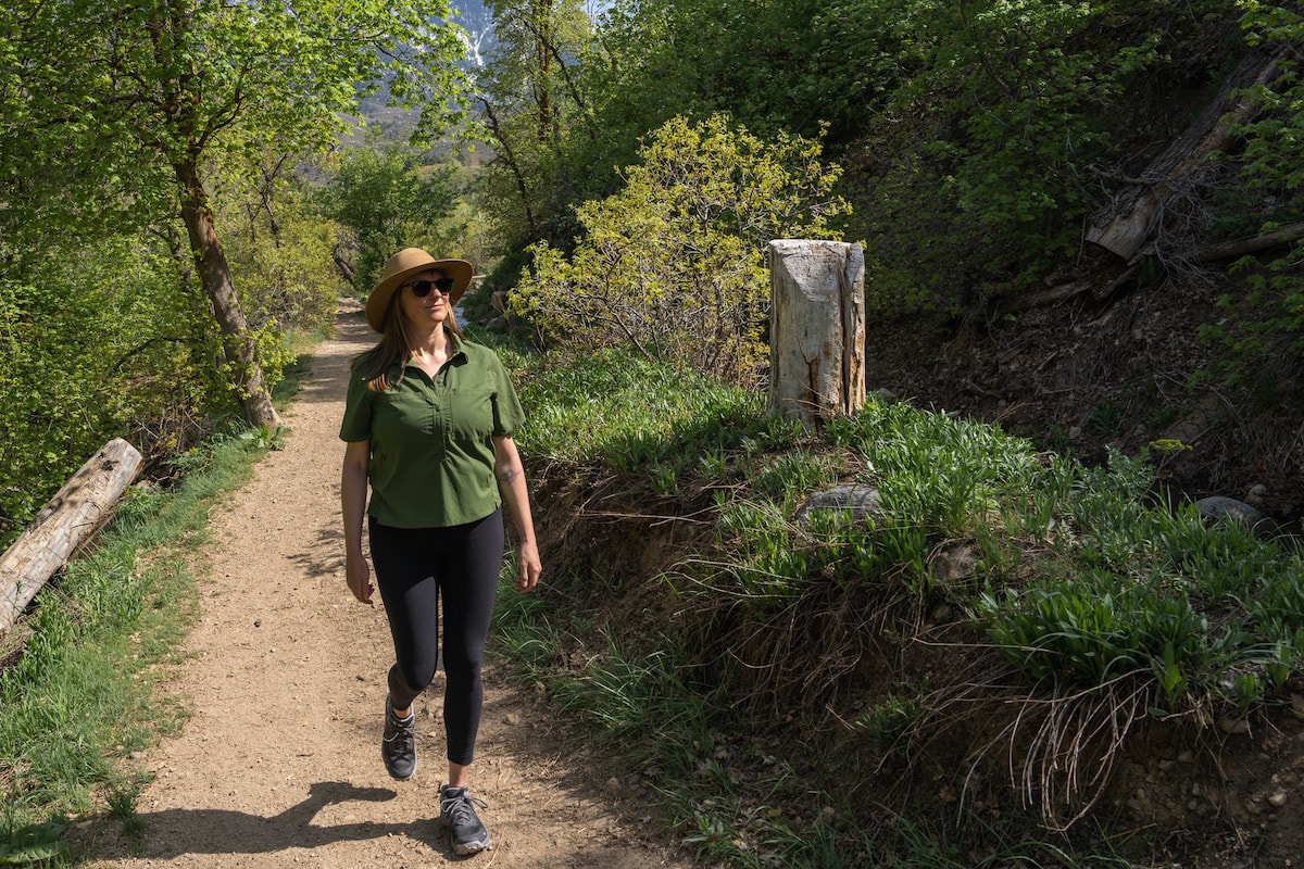 Kristen Bor hiking on a dirt trail with green trees and bushes around her.