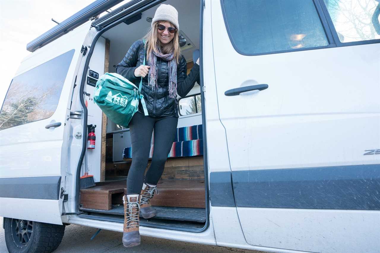 Kristen Bor on the edge of a Sprinter Van holding an REI Big Haul Duffel