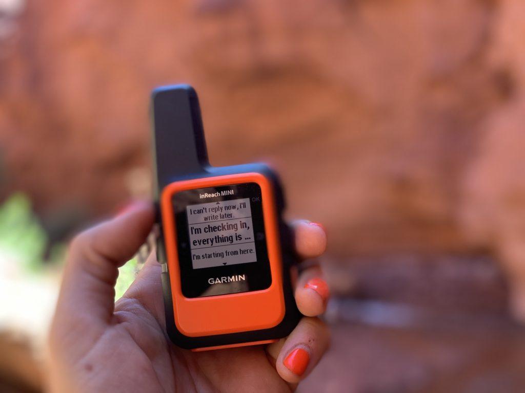 A close up of a hand holding a Garmin InReach Mini emergency communication device