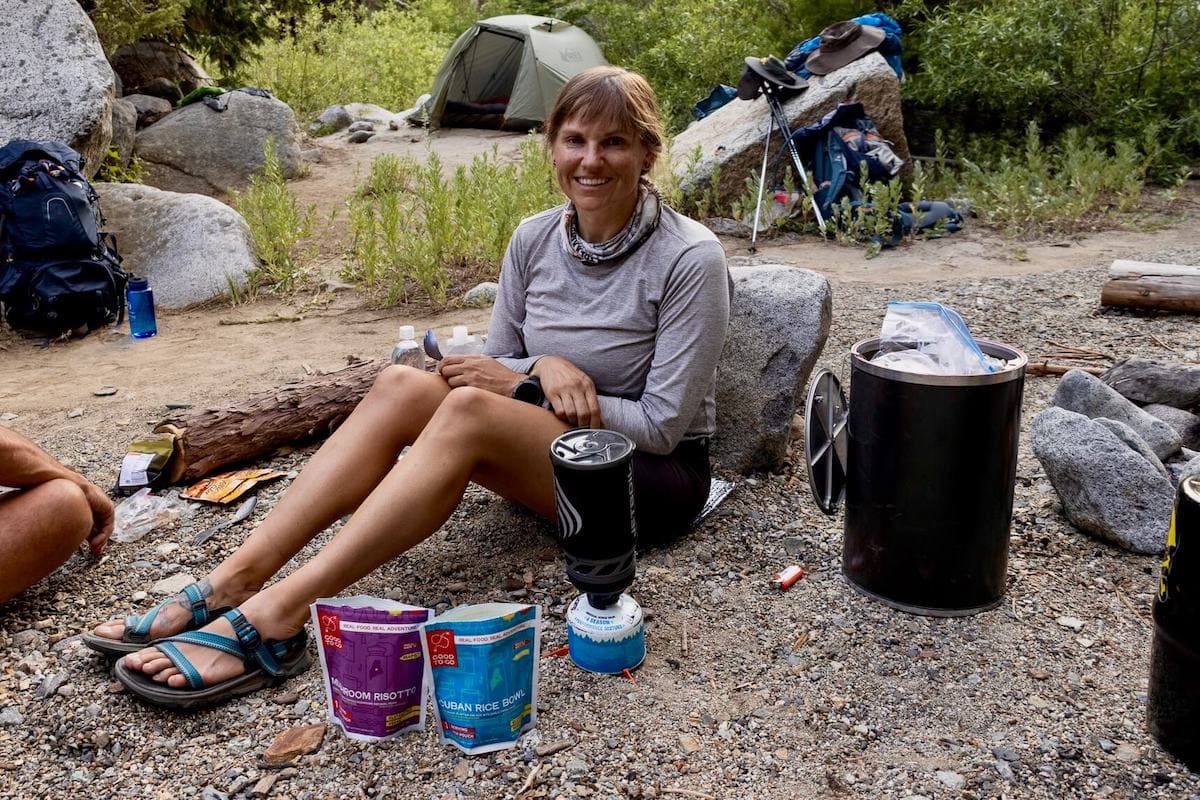 Kristen Bor sitting on ground next to backpacking stove and bear canister on backpacking trip