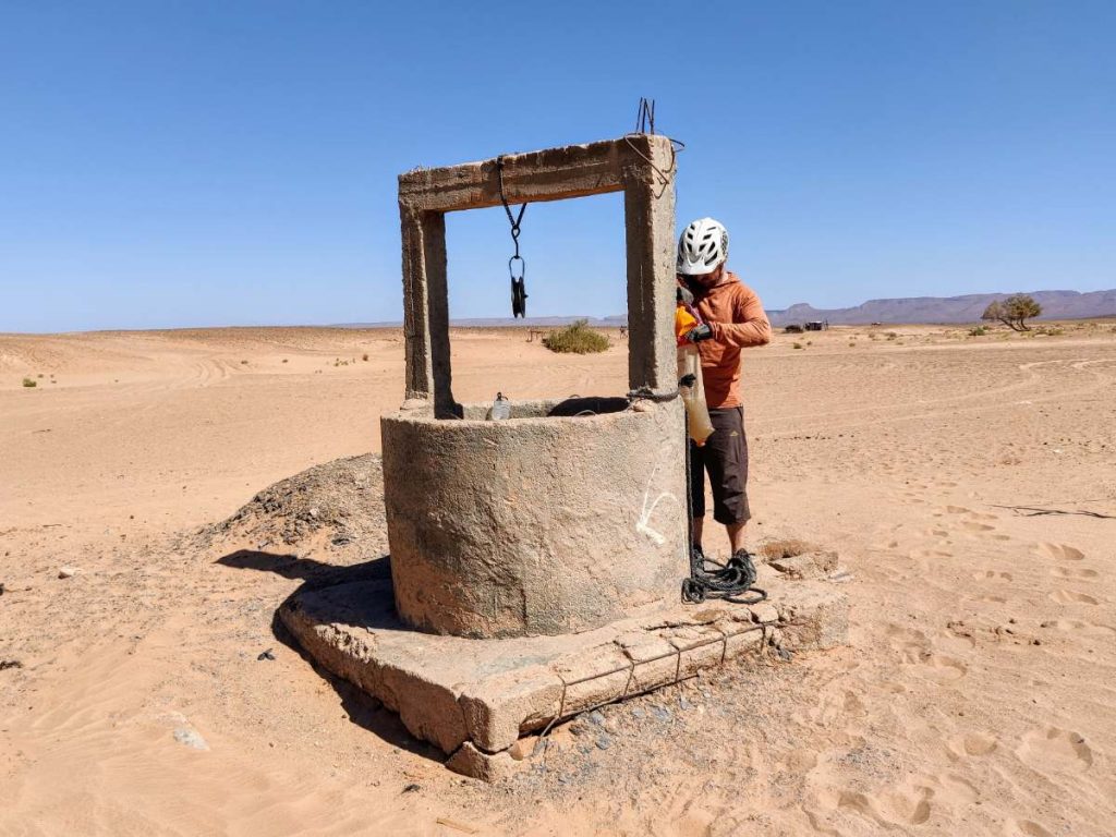 Man wearing bike helmet fills water bladder from well in desert