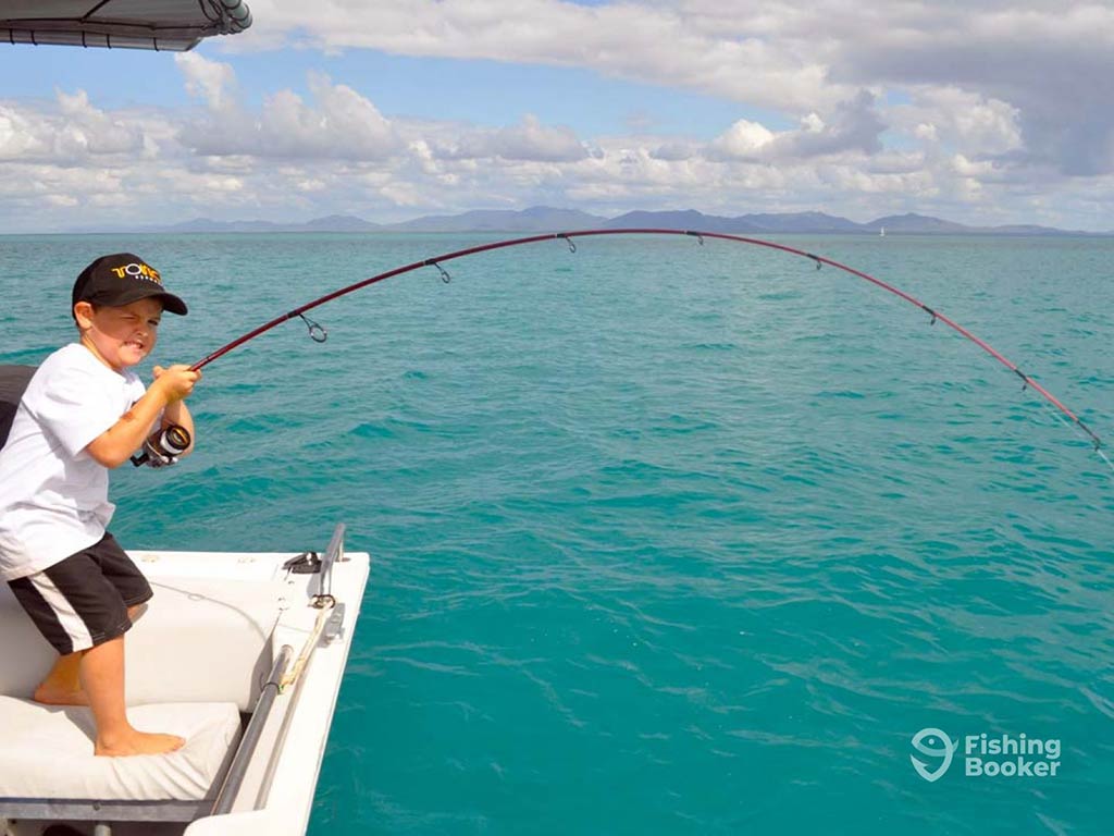 A young boy makes a face as though he's struggling, as he attempts to pull in a fish from the reefs in Airlie Beach