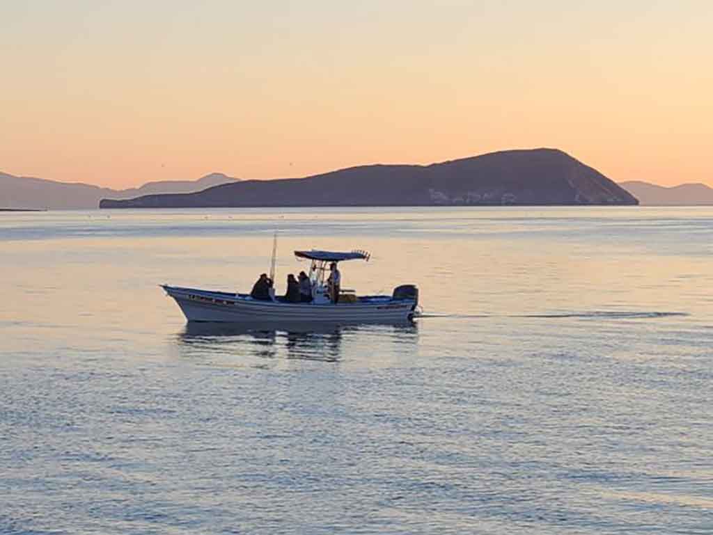 A view across the water towards a reef fishing charter in Baja California at sunset with a large hill visible in the distance