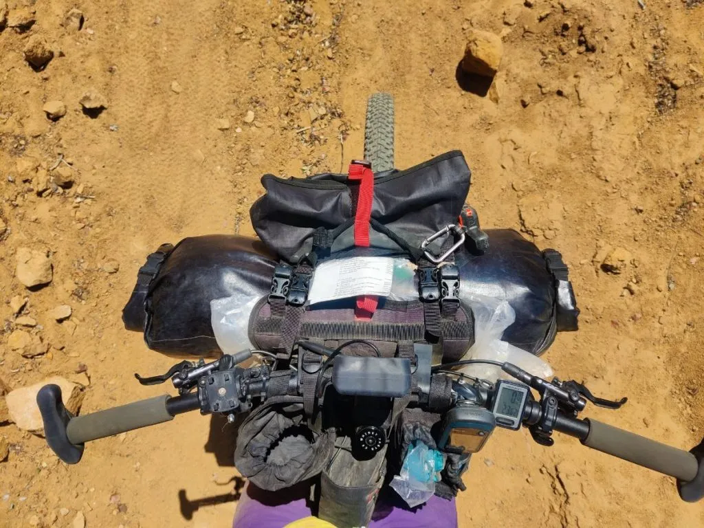 Looking down from rider's viewpoint on mountain bike handlebars loaded for bikepacking.