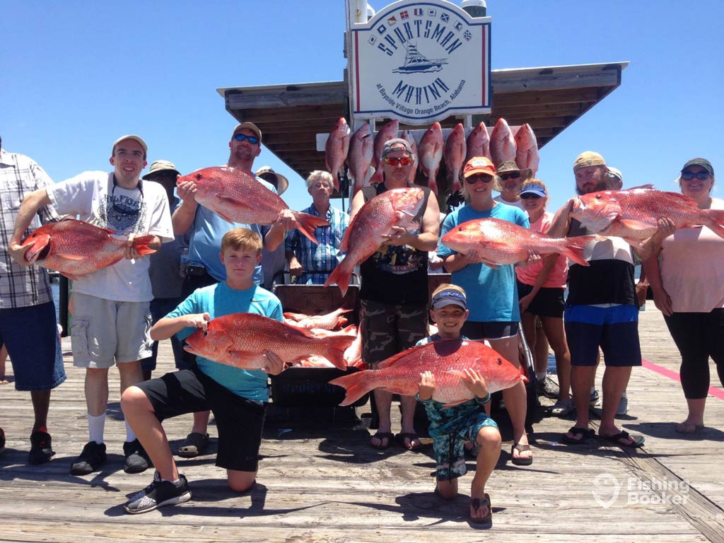 A photo featuring a group of almost 10 anglers posing with their catches on the dock after their fishing trip has finished and before they tip their fishing guide for a memorable experience
