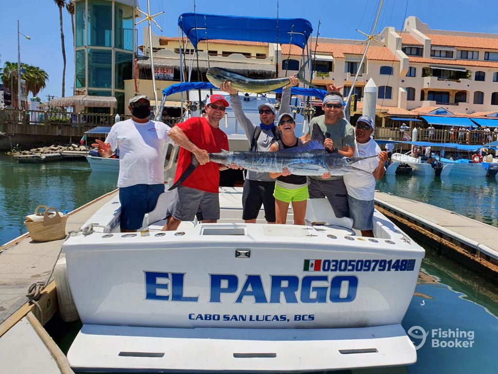 A photo showing a captain, his first mate, and several anglers posing together aboard a charter boat docked in the marina with a huge Billfish they caught during the deep sea fishing trip in Cabo San Lucas in Mexico