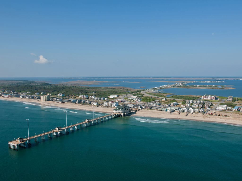 An aerial photo of the Outer Banks near Nags Head in North Carolina with afishing pier visible in the foreground and the sounds visible in the distance on a clear day