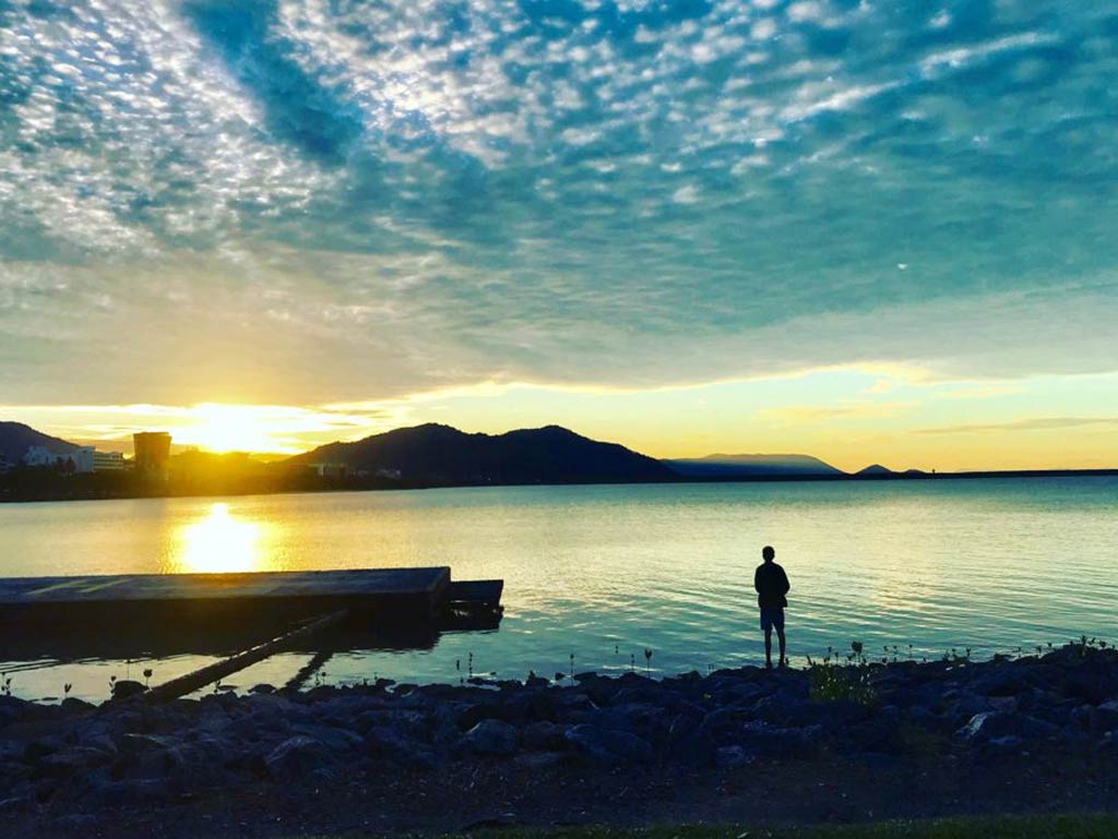 A photo of a lone angler standing on the shore and fishing at sunset in Queensland