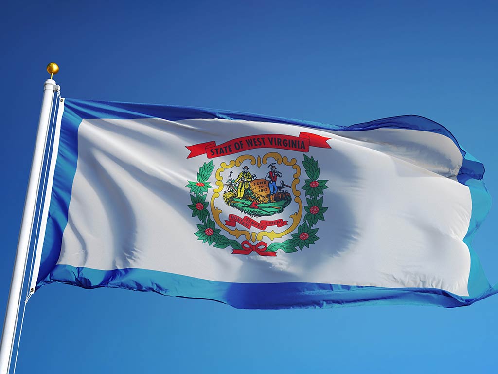 The flag of West Virginia flying from a flagpole against a background of a clear blue sky